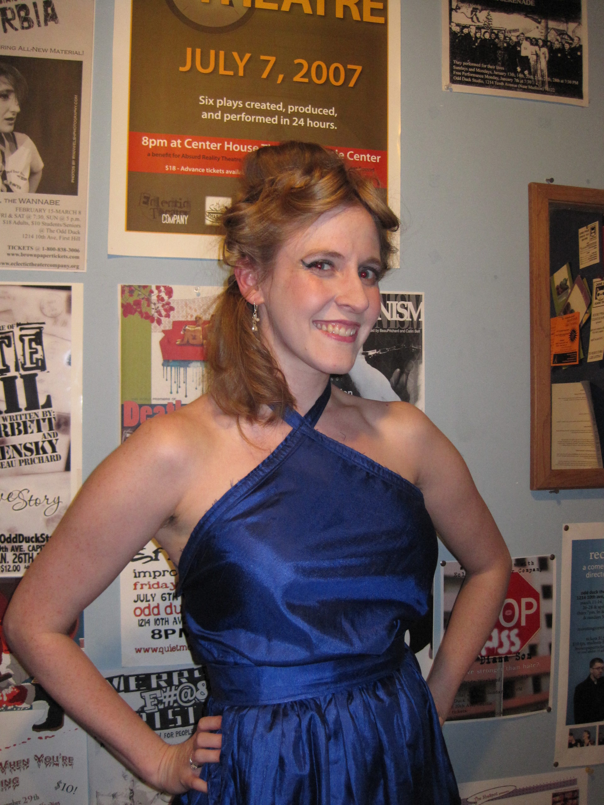 Cheryl poses in front of a wall of show posters with a space age hairdo and a blue halter dress.